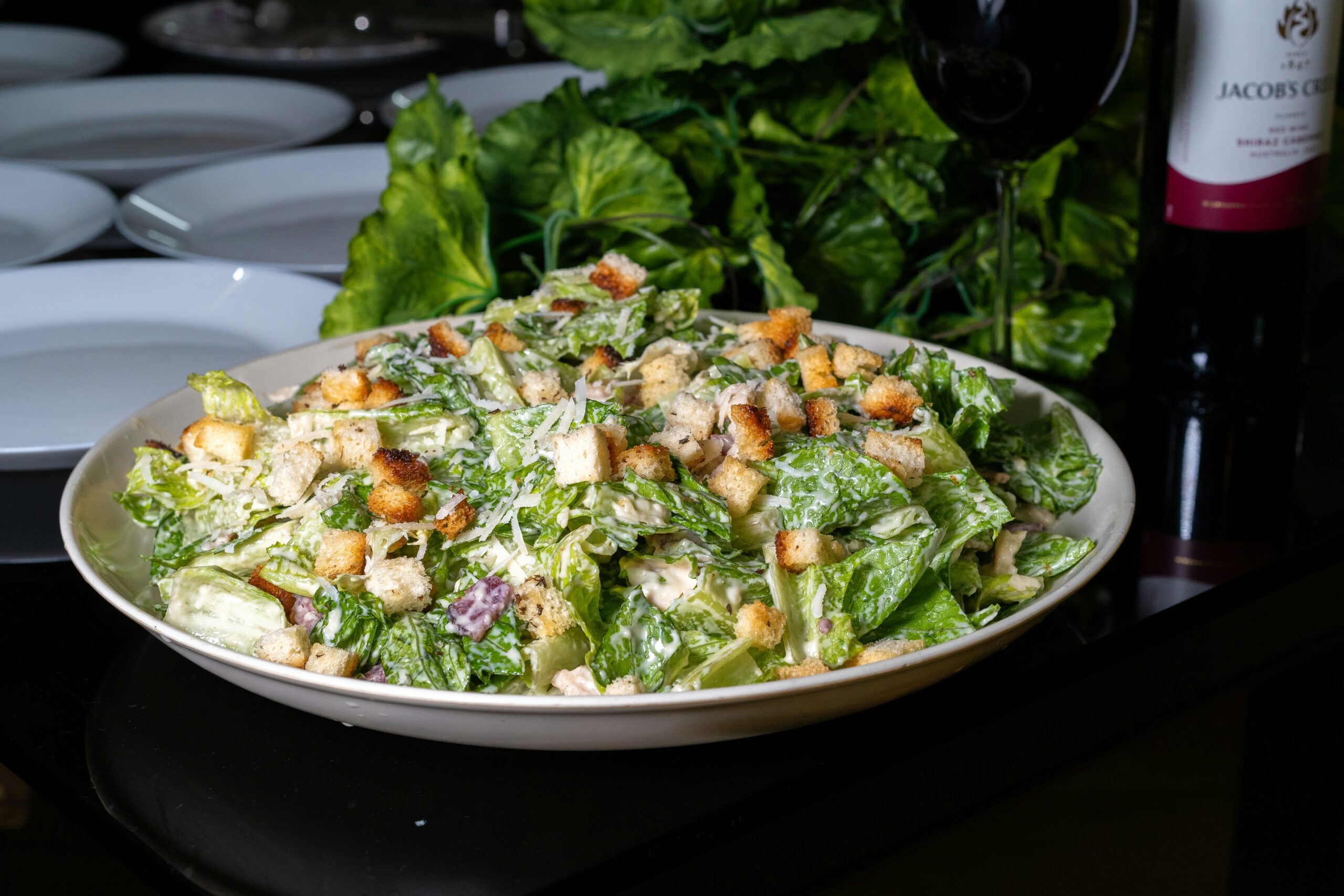 Grote schaal met romige vegan ceasar salade dressing, knapperige croutons en geraspte plantaardige kaas.