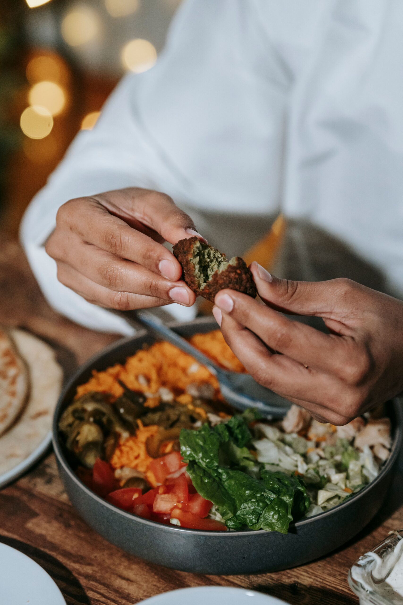 Persoon breekt falafel bolletje door midden boven een bord met goedkoopste vleesvervangers